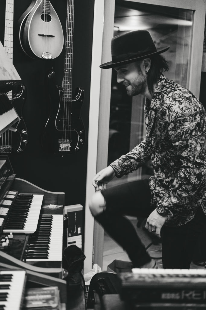 Black and white photo of Lukas Meijer in front of a keyboard in a hat and a patterned jacket